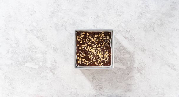 Flat lay. Filling square cheesecake pan lined with parchment paper with fudge mixture to prepare chocolate hazelnut fudge. - Photo, Image