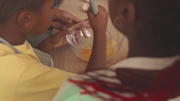 Abuela con dos nietos batiendo huevos en un tazón de vidrio mientras hace masa en casa - Metraje, vídeo