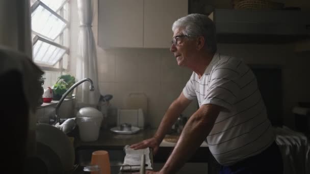 Kontemplativní starší muž stojící v kuchyni u okna v hlubokém mentálním rozjímání. Rozjímání o důchodci doma - Záběry, video