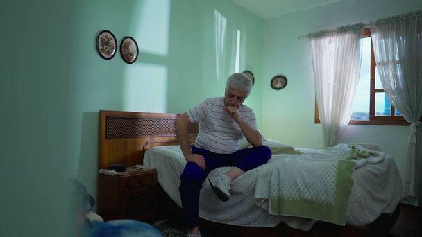 Figyelmes idős ember ül az ágy mellett a hálószoba komor elmélkedés. Az idős kort ábrázoló portré, dilemmával küszködő, töprengő döntés - Fotó, kép
