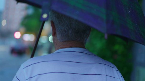 Dos de l'homme âgé marchant dans la rue tenant un parapluie pendant la journée de pluie. personne âgée mature se promener dans l'environnement urbain dans afternon sous la pluie - Photo, image
