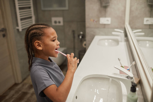 Oldalnézet portré a kis fekete lány fogmosás rózsaszín fogkefével jó fogászati higiéniai gyakorlat gyermekkorban - Fotó, kép