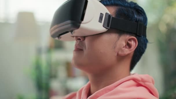 Κοντινό πλάνο του νεαρού άνδρα με μπλε μαλλιά σε VR-γυαλιά που παίζει online παιχνίδι ενώ κάθεται σε εσωτερικούς χώρους - Πλάνα, βίντεο