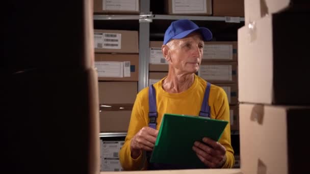 Warehouse manager oude werknemer schrijven op klembord in een groot magazijn. Kopieerruimte - Video