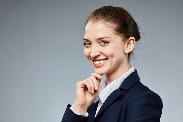 Portrait of smiling young businesswoman looking at camera while standing against grey background in studio, copy space - Photo, Image