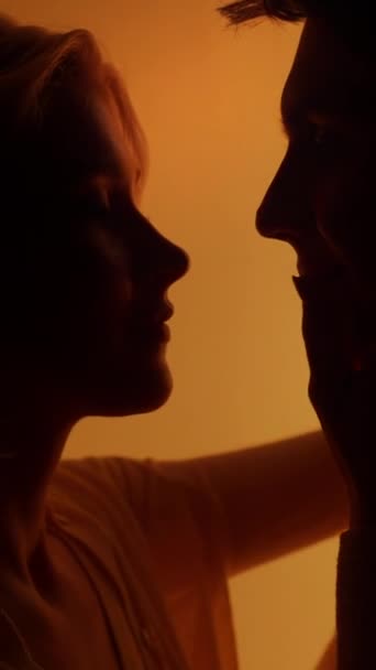 Κάθετη άποψη του νεαρού ζευγαριού φιλιούνται κατά τη διάρκεια ρομαντικής ημερομηνίας κάτω από έντονο πορτοκαλί φωτισμό νέον. Έννοια συναισθημάτων - Πλάνα, βίντεο