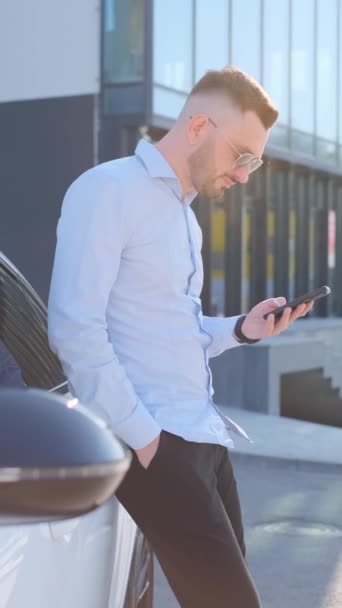 Vídeo vertical de un gerente con una camisa blanca hablando en un smartphone sobre el fondo de un centro de negocios. Concepto de negocio. Vídeo vertical - Imágenes, Vídeo