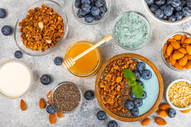 Bowl of granola with yogurt and fresh berries on a texture table. Yogurt berries, acai bowl, spirulina bowl. Healthy food, balanced breakfast. Strawberries, blueberries, kiwi, peach, almonds and chia.  - Photo, Image