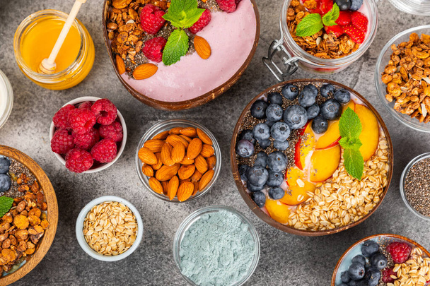 Bowl of granola with yogurt and fresh berries on a texture table. Yogurt berries, acai bowl, spirulina bowl. Healthy food, balanced breakfast. Strawberries, blueberries, kiwi, peach, almonds and chia.  - Photo, Image