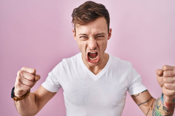 ピンクのバックグラウンドの上に立って怒り狂った男は怒りで叫んでいる間にフラストレーションと激怒した. 怒りと攻撃的な概念.  - 写真・画像