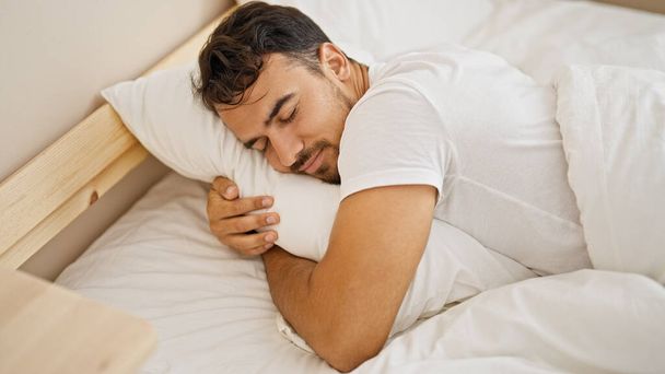 Junger hispanischer Mann umarmt auf Bett liegendes Kissen und schläft im Schlafzimmer - Foto, Bild