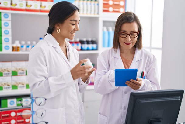 Two women pharmacist using touchpad holding pills at pharmacy - Photo, Image