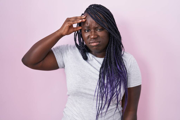 Mujer africana joven de pie sobre fondo rosa preocupada y estresada por un problema con la mano en la frente, nerviosa y ansiosa por la crisis  - Foto, imagen
