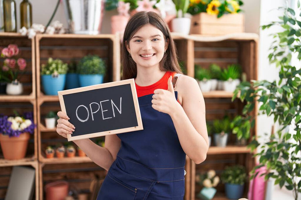 Young caucasian woman working at florist holding open sign smiling happy and positive, thumb up doing excellent and approval sign  - Photo, Image