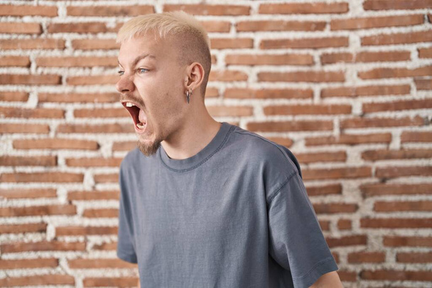 Młody biały mężczyzna stojący nad murem wściekły i wściekły krzyczący sfrustrowany i wściekły, krzyczący ze złości. wściekłość i agresywne pojęcie.  - Zdjęcie, obraz