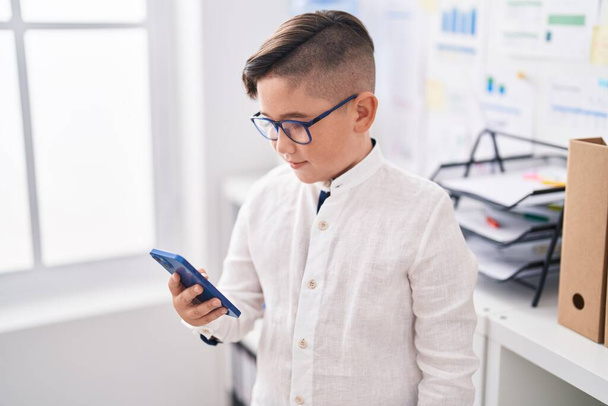 Imádnivaló spanyol fiú üzletember mosolygós magabiztos segítségével smartphone az irodában - Fotó, kép