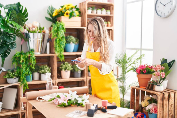 Young blonde woman florist make photo to flowers by smartphone at florist - Fotoğraf, Görsel
