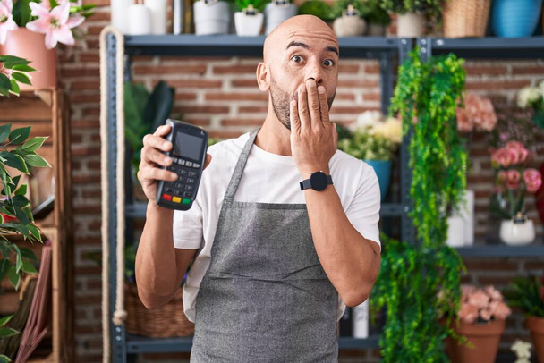Keski-ikä kalju mies työskentelee kukkakauppa tilalla dataphone peittää suun käsin, järkyttynyt ja pelkää virhe. yllättynyt ilme  - Valokuva, kuva