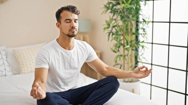 Young hispanic man doing yoga exercise sitting on bed at bedroom - Photo, Image