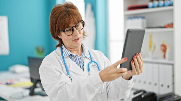 Femme d'âge moyen médecin faisant appel vidéo avec pavé tactile à la clinique - Photo, image