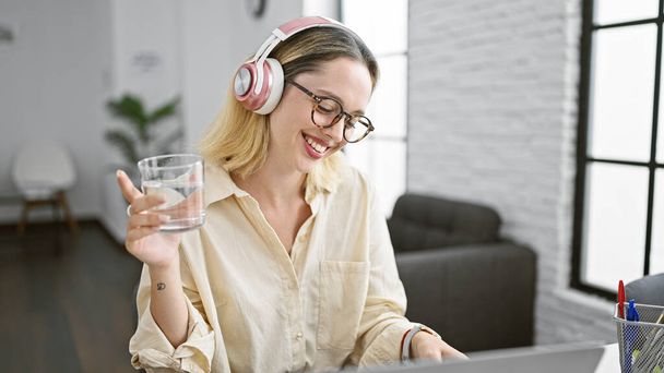 Młoda blondynka biznes pracownik słuchanie muzyki wody pitnej w biurze - Zdjęcie, obraz