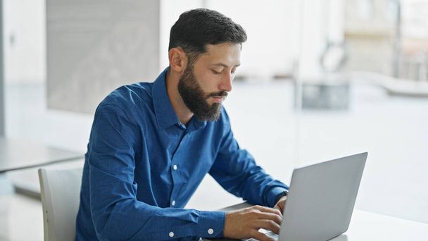 Jonge Spaanse zakenman die laptop gebruikt die op kantoor werkt - Foto, afbeelding