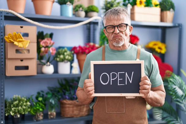 Hispanic man with grey hair working at florist holding open sign skeptic and nervous, frowning upset because of problem. negative person.  - Photo, Image