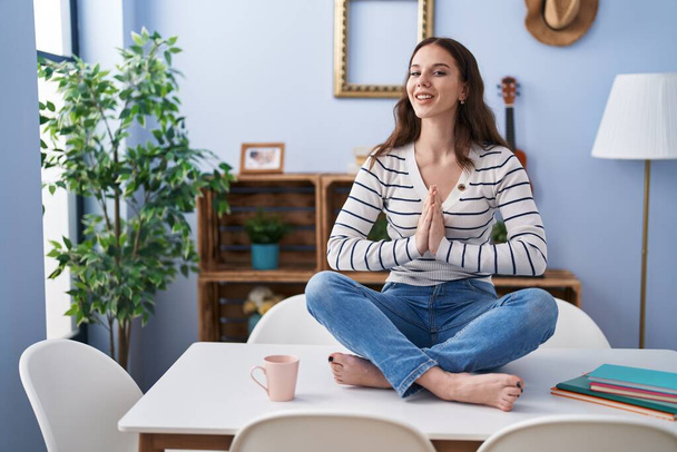 Young woman doing yoga exercise sitting on table at home - Foto, imagen