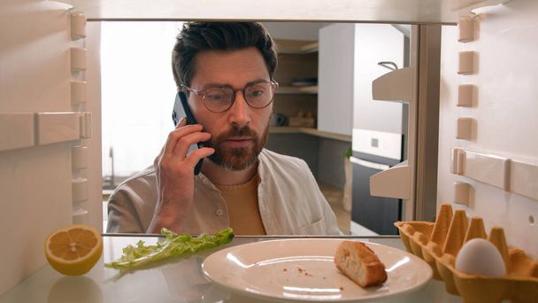 Näkökulma POV sisällä jääkaappi Valkoihoinen mies kaveri auki jääkaappi yksi muna salaatti lehtiä pala leivänmuruja tyhjä pullo mehua puhuminen puhelin tilata tuotteita soita ruoka toimitus palvelu - Valokuva, kuva
