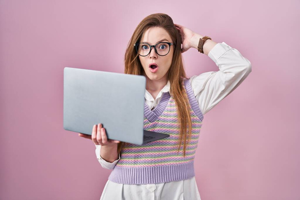 Młoda kaukaska kobieta pracuje przy użyciu komputera laptop szalony i przestraszony z rękami na głowie, boi się i zaskoczony szoku z otwartymi ustami  - Zdjęcie, obraz