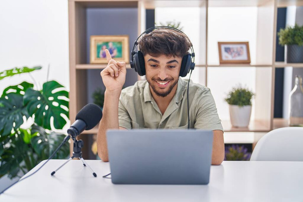 Arabe avec barbe travaillant à la radio souriant heureux pointant avec la main et le doigt sur le côté  - Photo, image