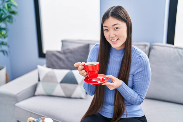 Китаянка пьет кофе сидя дома на диване - Фото, изображение