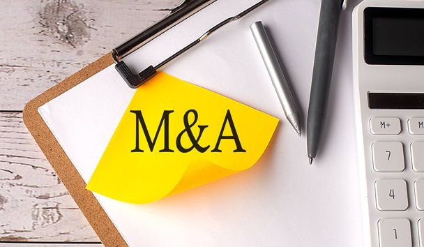 M και μια λέξη σε ένα κίτρινο κολλώδες με αριθμομηχανή, στυλό και πρόχειρο - Φωτογραφία, εικόνα