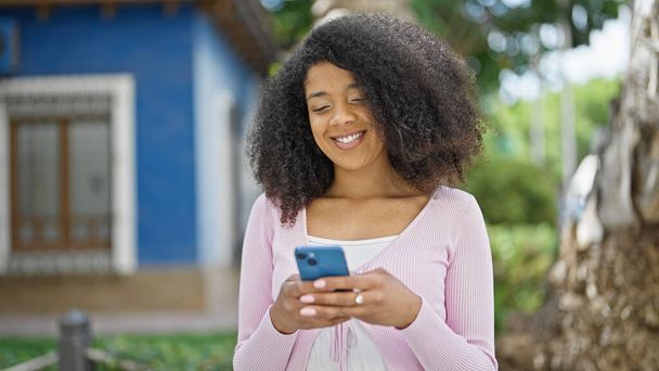 Afroamerykanka korzystająca ze smartfona uśmiechnięta w parku - Zdjęcie, obraz