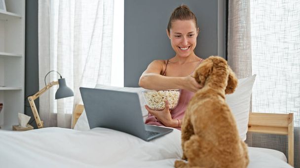 Jeune femme caucasienne avec chien regarder film sur ordinateur portable assis sur le lit dans la chambre - Photo, image