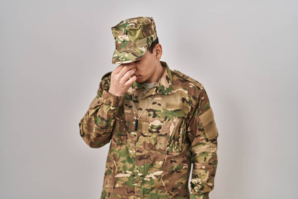 Młody arabski mężczyzna w mundurze wojskowym, zmęczony pocieraniem nosa i oczu, odczuwający zmęczenie i ból głowy. koncepcja stresu i frustracji.  - Zdjęcie, obraz