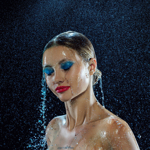 Portrait of wet young girls face. Drops of water running on her face with closed eyes with bright and colorful makeup over black background. Concept of beauty, fashion, art, halth, skin care. Ad. - Photo, Image