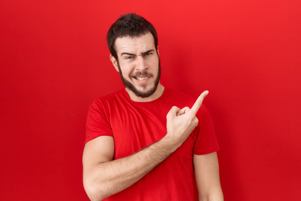 Nuori latinomies yllään rento punainen t paita osoittaa syrjään huolissaan ja hermostunut etusormi, huolissaan ja yllättynyt ilme  - Valokuva, kuva