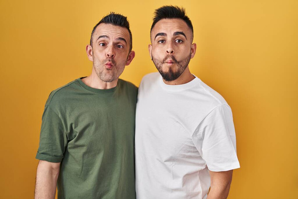 Homosexuální pár stojící nad žlutým pozadím dělá rybí obličej se rty, šílené a komické gesto. legrační výraz.  - Fotografie, Obrázek
