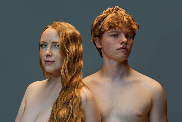 Couple. Shirtless serious man and cheerful woman with red hairs and freckles looking at camera over grey studio background. Concept of natural beauty, love, relationships, fashion. Ad. - Photo, Image