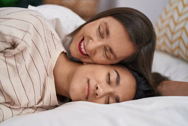 Twee vrouwen moeder en dochter glimlachen zelfverzekerd liggend op bed in de slaapkamer - Foto, afbeelding