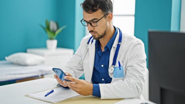 Молодий іспаномовний лікар використовує смартфон, що працює в клініці
 - Фото, зображення