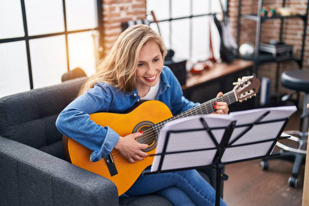 Νεαρή ξανθιά γυναίκα μουσικός παίζει κλασική κιθάρα στο στούντιο μουσικής - Φωτογραφία, εικόνα