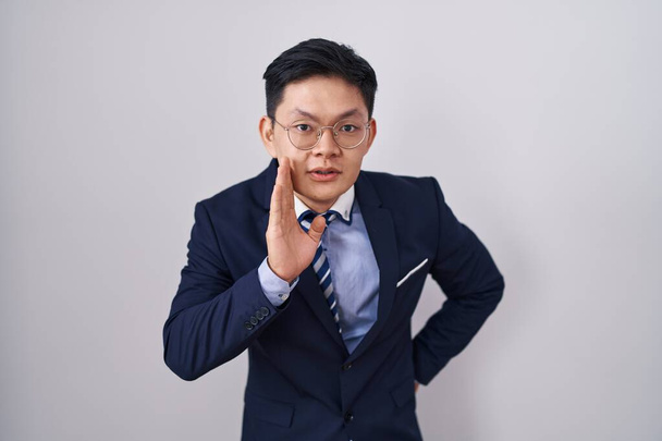 Giovane asiatico uomo indossare business suit e cravatta mano sulla bocca dicendo segreto rumor, sussurrando malizioso conversazione  - Foto, immagini