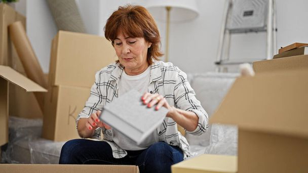Mujer de mediana edad desembalaje caja de cartón en el nuevo hogar - Foto, imagen