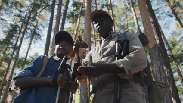 Alacsony szög kilátás közepes lövés afro-amerikai idős férfi és unokája túrázás a hegyekben a nyári napon segítségével iránytű - Felvétel, videó