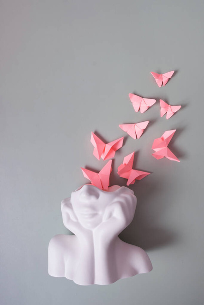 Una statuetta di testa con farfalle rosa su sfondo grigio. Concetto di salute mentale. - Foto, immagini
