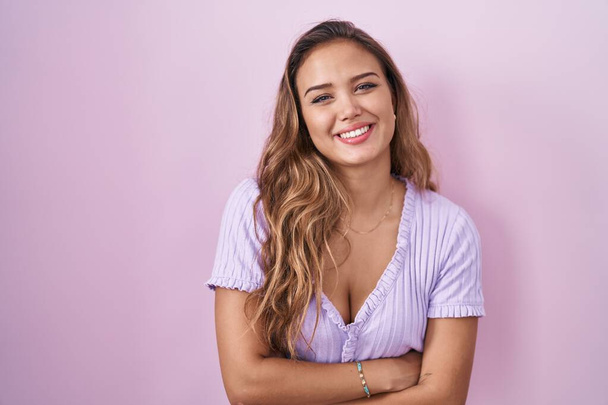 Junge hispanische Frau vor rosa Hintergrund glücklich lächelnd mit verschränkten Armen in die Kamera blickend. positive person.  - Foto, Bild