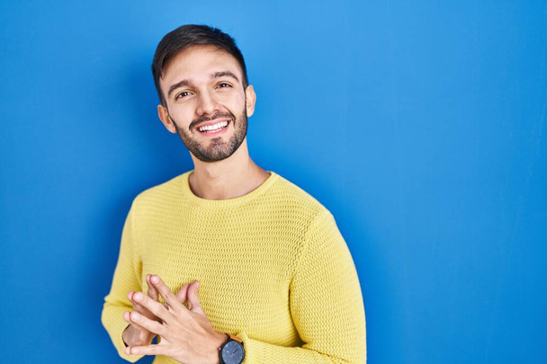 Hombre hispano de pie sobre fondo azul manos juntas y dedos cruzados sonriendo relajado y alegre. éxito y optimismo  - Foto, Imagen