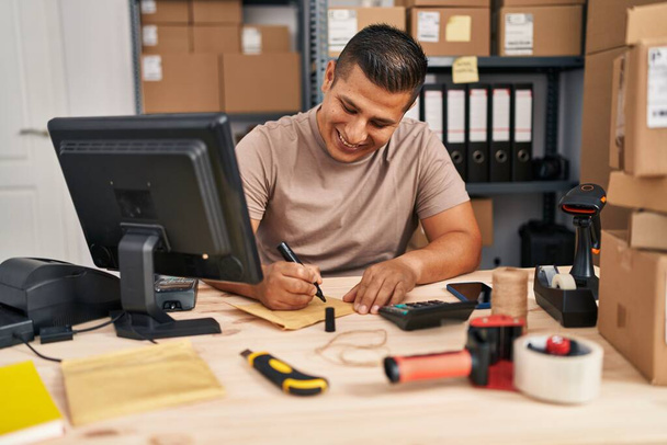 Молодий латинський чоловік електронної комерції бізнесмен пише на упаковці в офісі
 - Фото, зображення